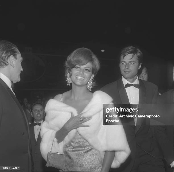 Italian actress Claudia Cardinale, wearing a fur and prescious earrings, portrayed during an evening party with Jean Sorel, Lido, Venice, 1965.