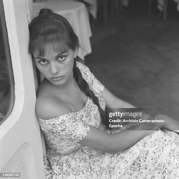 Italian actress Claudia Cardinale, portrayed while sitting on the floor, wearing a plait and a floral dress, Venice, 1958.