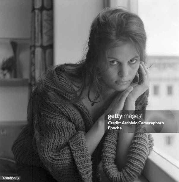 Italian actress Claudia Cardinale portrayed while wearing a woolen jumper, sitting close to a window, Rome, 1959.