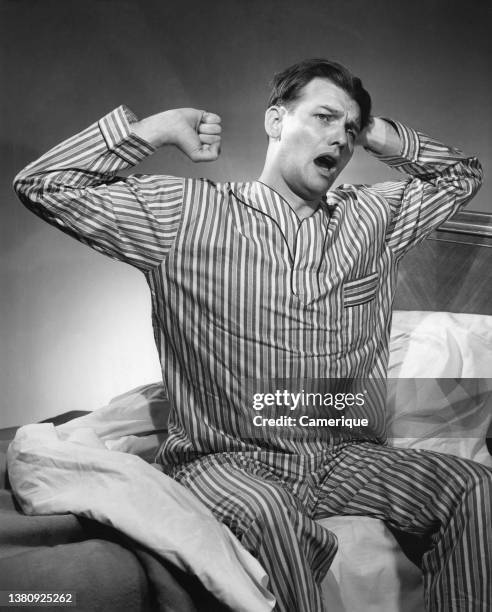 Man in PJ's sitting up in bed stretching after waking up.