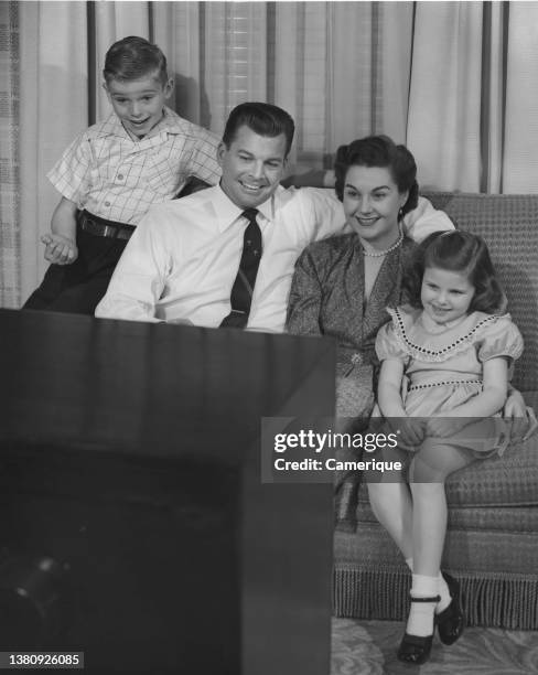 Well-dressed family of Mom, Dad, boy and girl sitting on the couch watching TV.