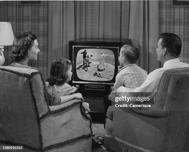 Well dressed family of Mom, Dad, boy and girl sitting watching baseball game on Television.