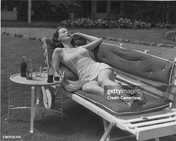 Woman laying outside enjoying the sunshine with Coca Cola bottles on table next to her.