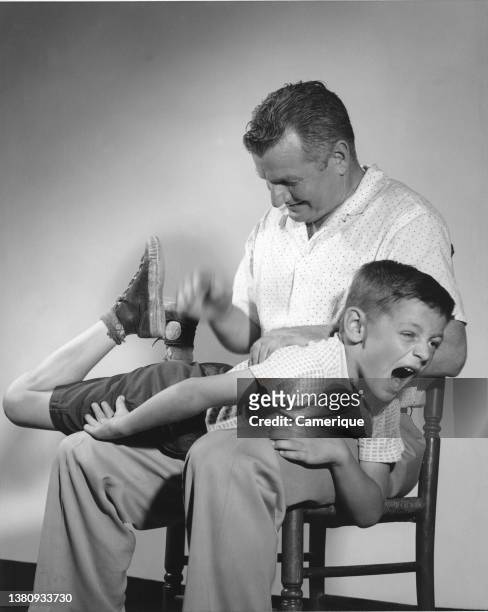 Dad spanking his son who is draped over his lap yelling in pain.
