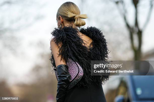 Leonie Hanne wears black and rhinestones YSL pendant earrings from Saint Laurent Paris, a black V-neck /feathers shoulders / short dress, black shiny...