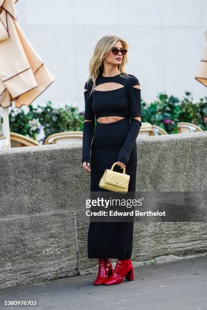 Xenia Adonts wears black vintage sunglasses, silver earrings, a black cut-out chest and waist long dress, a pale yellow quilted leather handbag from...