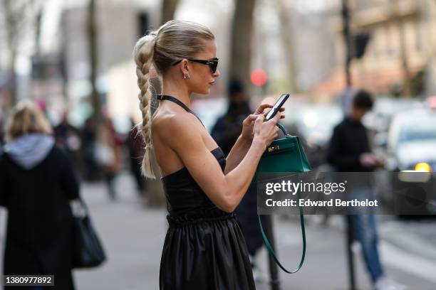 Caroline Daur wears black cut-out sunglasses from Loewe, silver and rhinestones earrings, a black shiny leather halter-neck / shoulder-off /...