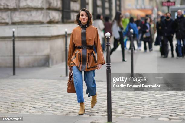 Alexandra Pereira wears gold and silver hair clips, gold and silver earrings, a camel with dark brown shiny leather borders / high neck / flared...