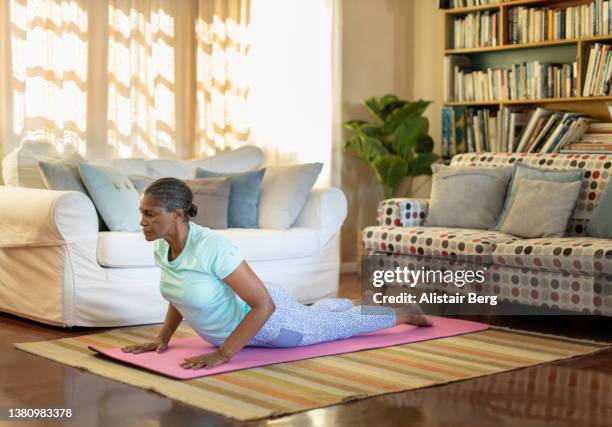 mature woman doing yoga exercises in her home - zen-like stock pictures, royalty-free photos & images
