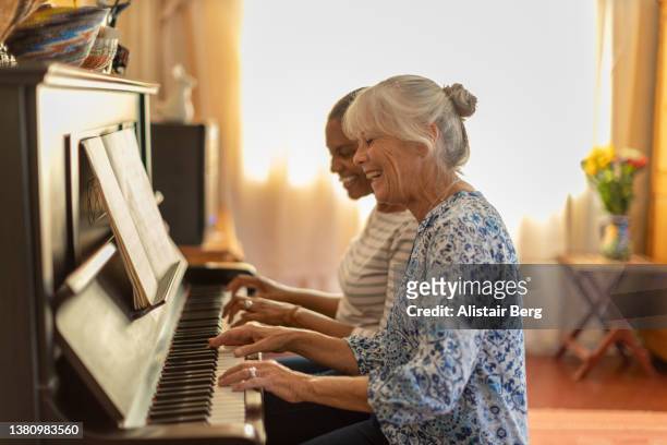 two women playing the piano together at home - retirement fun stock pictures, royalty-free photos & images