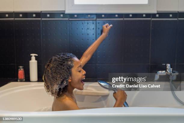 boy sitting in bath singing into a shower head - boy taking a shower stock-fotos und bilder