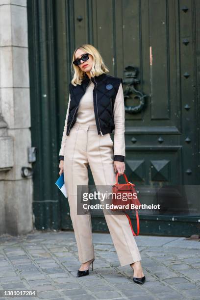 Candela Novembre wears black sunglasses, a black quilted sleeveless puffer jacket, a beige leather jacket, matching beige leather pants, an orange...