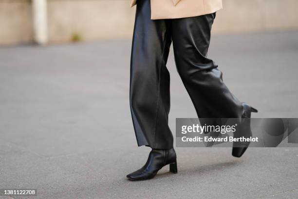 Guest wears a beige belted jacket, black shiny leather large pants, black shiny leather block heels ankle boots, outside Hermes , during Paris...