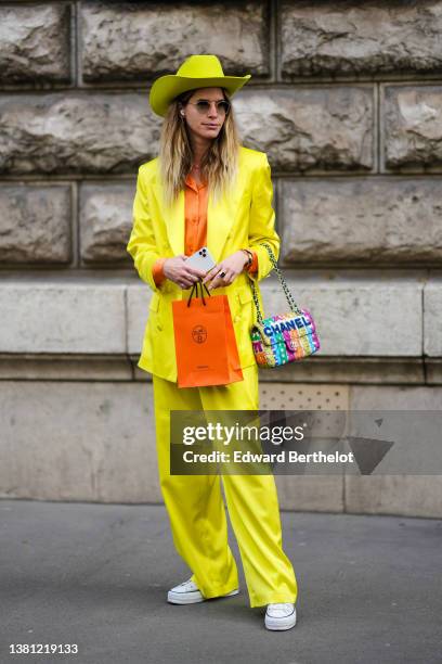 Guest wears a yellow felt / wool cow-boy hat, sunglasses, a pink / blue colored necklace, an orange shirt, a yellow blazer jacket, matching yellow...