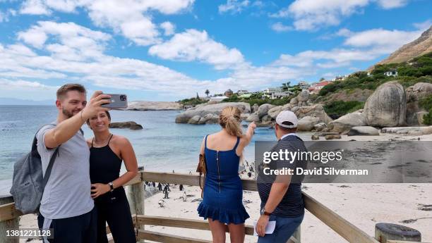 Tourists photograph themselves and the African Penguins that inhabit the Boulders Penguin Colony, part of the Table Mountain National Park, on...