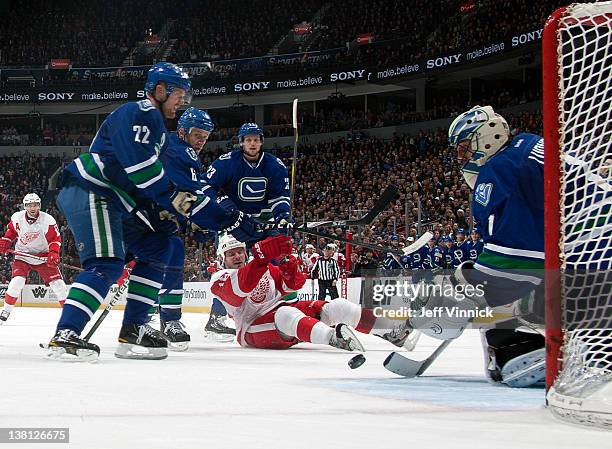 Ian White of the Detroit Red Wings is surrounded by Daniel Sedin, Roberto Luongo, Sami Salo and Alexander Edler of the Vancouver Canucks during a NHL...