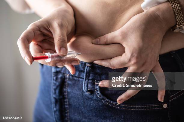 woman holds her belly skin while applying insulin shot by an injection. - injecteren stockfoto's en -beelden