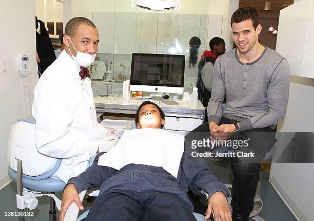 Kris Humphries looks on as Dr. Lee Gause DDS performs dental care on Tariq of Urban Promise during Celebrities For Smiles hosted by Kris Humphries at...