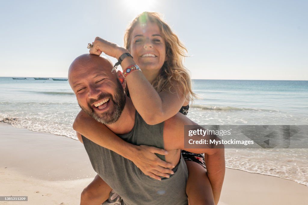 Couple playing piggyback on the beach at sunset or sunrise