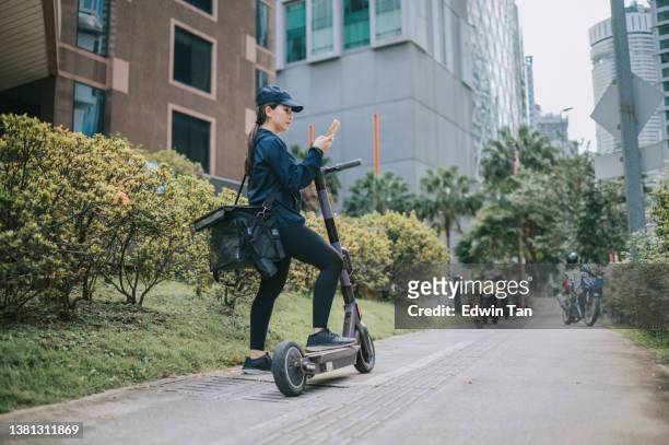 repartidora asiática china que verifica la dirección del pedido en movimiento con el scooter eléctrico como modo de transporte en la ciudad - huella de carbono fotografías e imágenes de stock