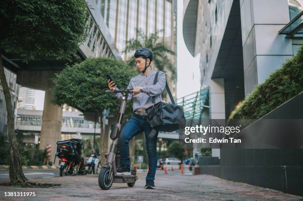 asian chinese male delivery person checking order address on the move with electric push scooter as mode of transport in city - bicycle messenger stock pictures, royalty-free photos & images