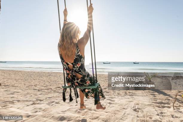 young woman having fun swinging on the beach at sunrise - swing stock pictures, royalty-free photos & images