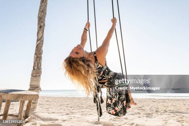 young woman having fun swinging on the beach at sunrise - swinging stock pictures, royalty-free photos & images