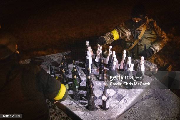 Members of a Territorial Defence unit play checkers with molotov cocktails while guarding a barricade after curfew on the outskirts of eastern Kyiv...