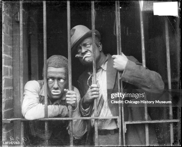 Radio actors, Charles J. Correll and Freeman Gosden of Amos 'n Andy, wearing blackface and costumes standing behind an iron gate in a building,...