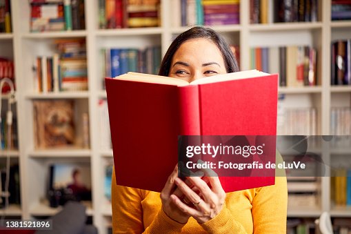 Female young behind book with face covered for a red book while smiling Female young behind book with face covered for a red book while smiling