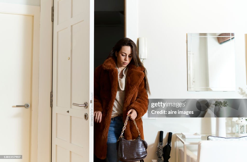 Beautiful long-haired woman arriving home after work, dressed in cold weather coat and fashionable clothes.