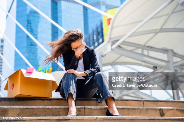 depressed businesswoman being fired by company downsizing sitting with carrying box of personal items in the city - smart numbers office stockfoto's en -beelden