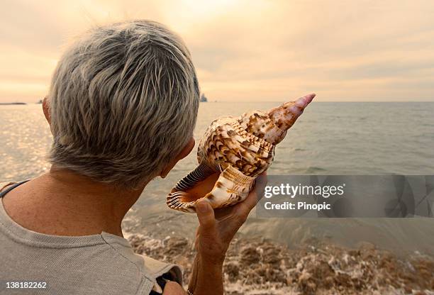 woman holding a conch as listening the sea - conch shell stockfoto's en -beelden