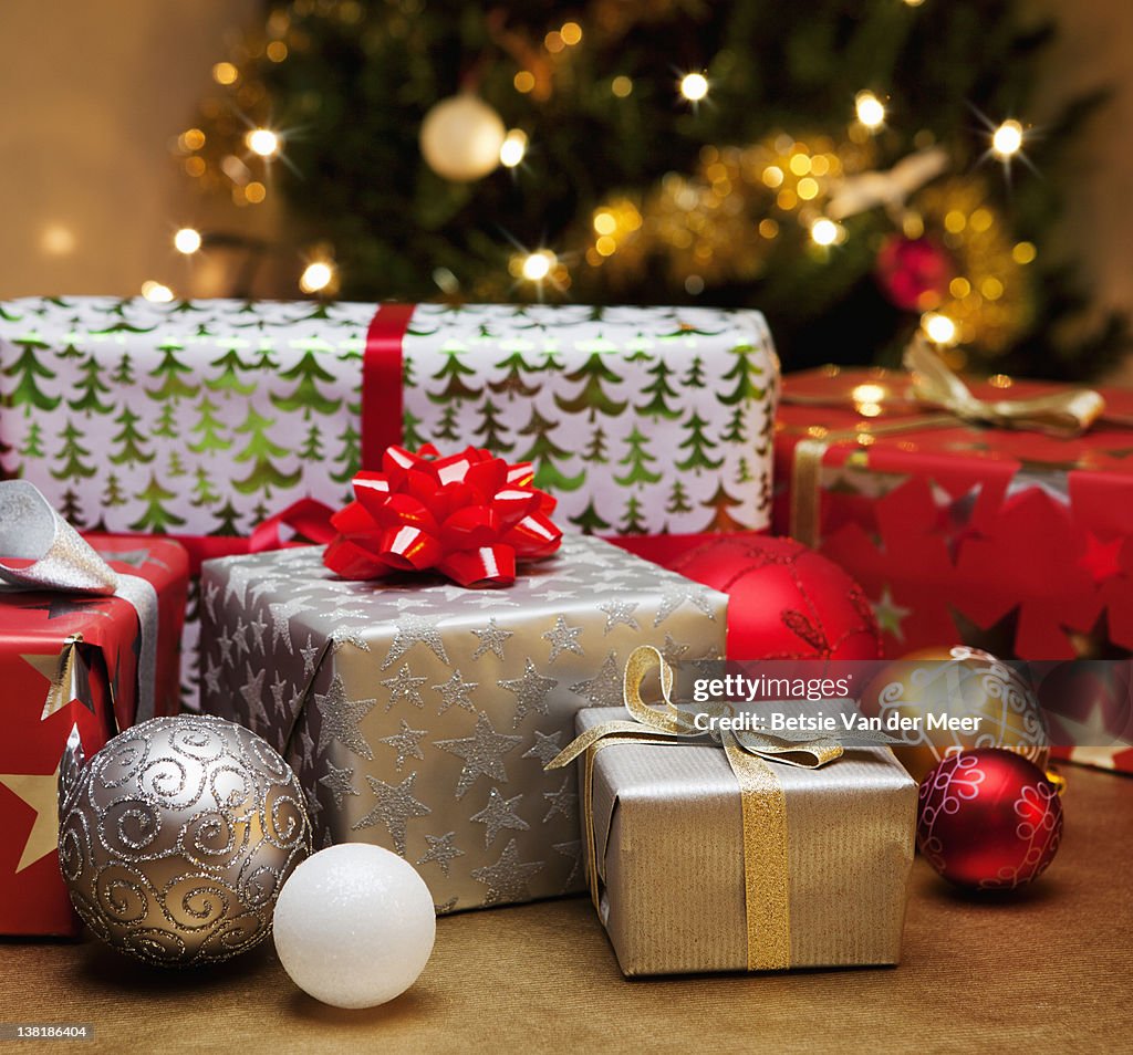 Christmas gifts and baubles in front of tree.