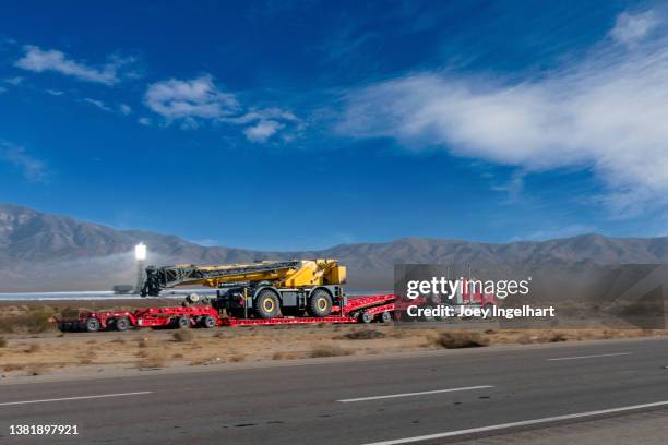 semi-remorque tractant un gros déménageur de terre sur une autoroute à quatre voies près de l’installation d’énergie solaire d’ivanpah - skirt stock photos et images de collection