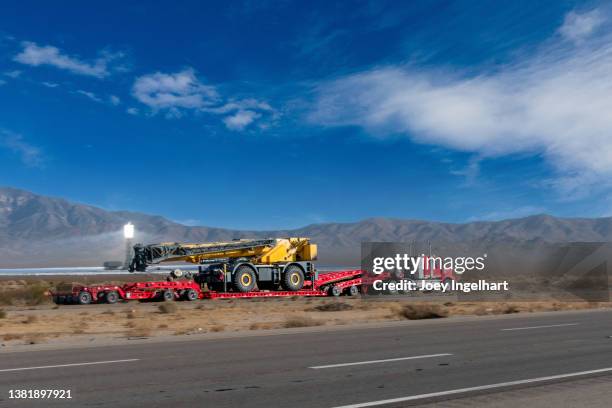 semi truck hauling a large dirt mover on a four lane highway near the ivanpah solar power facility - heavy equipment stock pictures, royalty-free photos & images