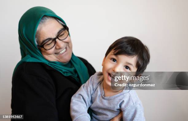 senior woman wearing a green headscarf playing with her grandson at home - headwear photos stock pictures, royalty-free photos & images