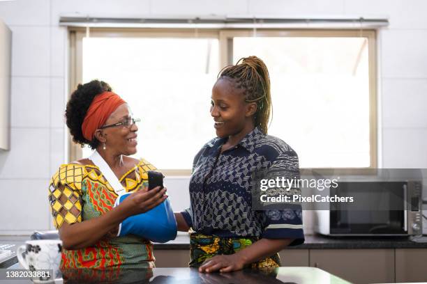 woman with injured arm shows adult daughter phone screen - african injured stock pictures, royalty-free photos & images