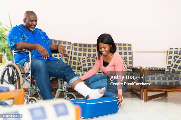 woman puts a cushion under senior man's injured foot - african injured stock pictures, royalty-free photos & images