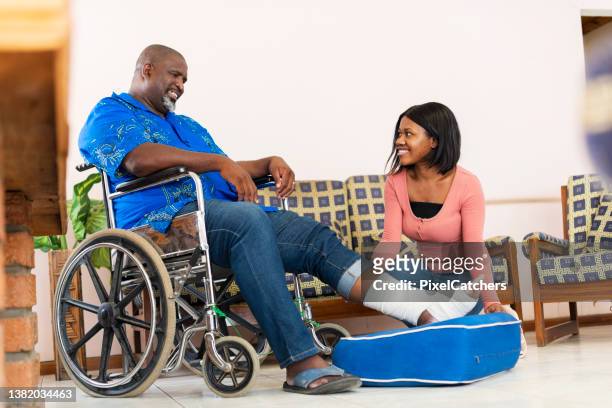 young woman taking care of senior man at home with injured foot - african injured stock pictures, royalty-free photos & images