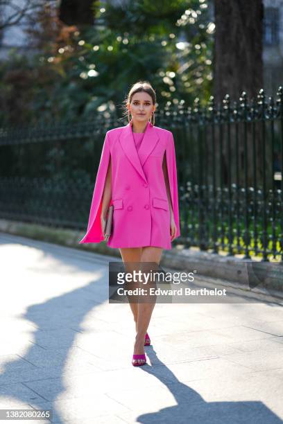 Diane Batoukina wears gold oversized earrings, a pink dress, a pink matching blazer jacket cloak, a brown matte leather nailed clutch from Valentino,...