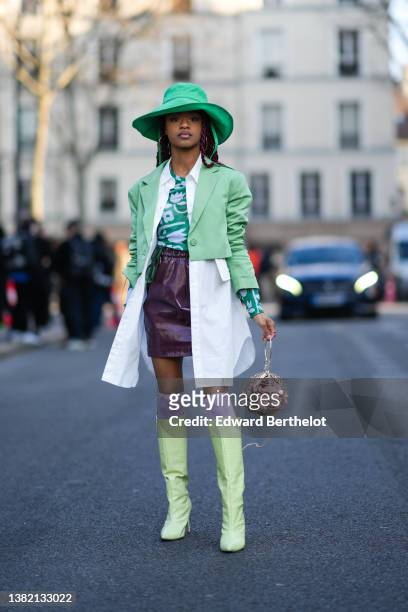 Debbie @blackhey wears a green oversized coat, gold earrings, a green with white flower print pattern t-shirt, a white long shirt, a pale green...