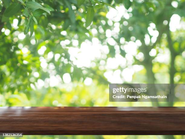 brown wooden table on blurred greenery nature background, natural template foliage green leaves texture backlight bokeh sunshine for display product - plank meubels photos et images de collection