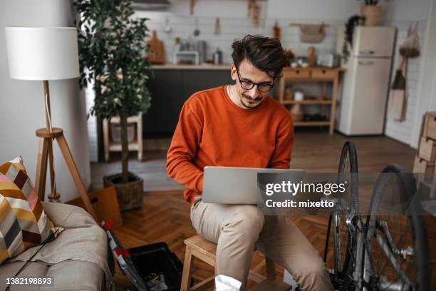 young man with laptop crouching by bicycle at home - damaged laptop stock pictures, royalty-free photos & images