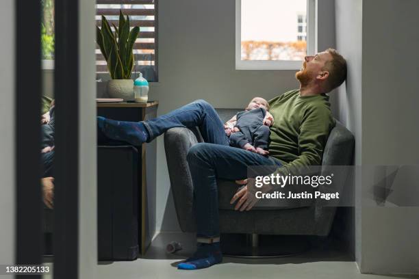 mature man sleeps on the armchair whilst he holds his baby daughter - feet up stock pictures, royalty-free photos & images