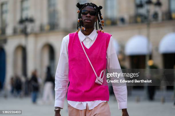 Guest wears silver and orange pearls in the hair, black sunglasses, a white shirt, a neon pink wool sleeveless pullover, a pink and white crocodile...