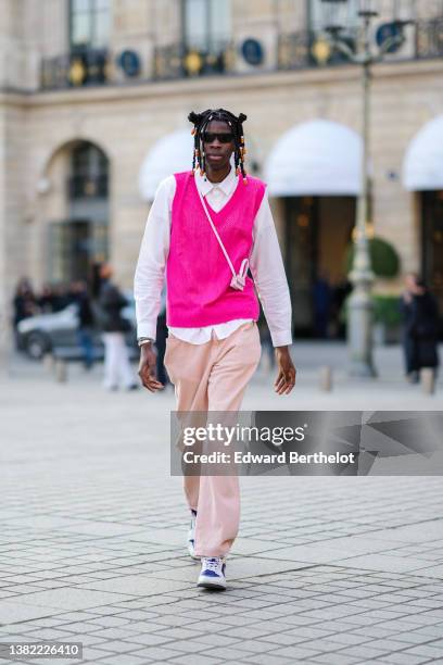 Guest wears silver and orange pearls in the hair, black sunglasses, a white shirt, a neon pink wool sleeveless pullover, a pink and white crocodile...