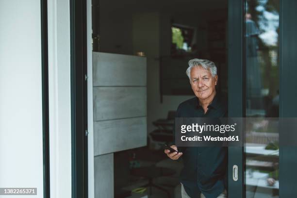 senior man with smart phone standing at doorway - old rich man stock pictures, royalty-free photos & images