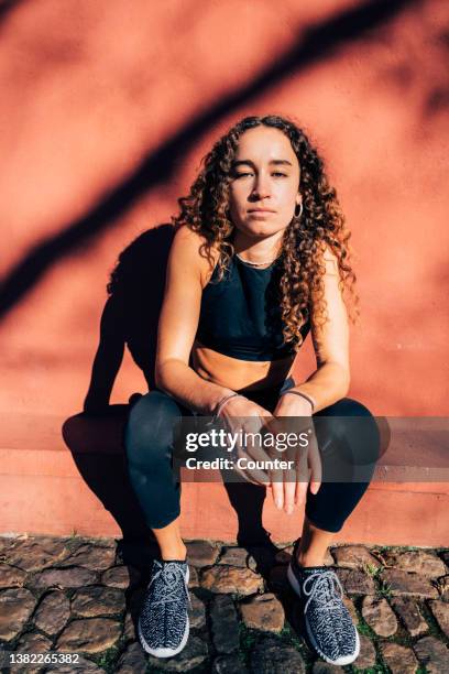 portrait of young woman sitting in front of red wall - sportlerin stock-fotos und bilder