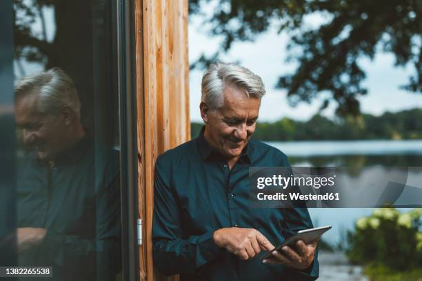 smiling senior man using tablet pc by glass wall at backyard - mann vor pc stock-fotos und bilder